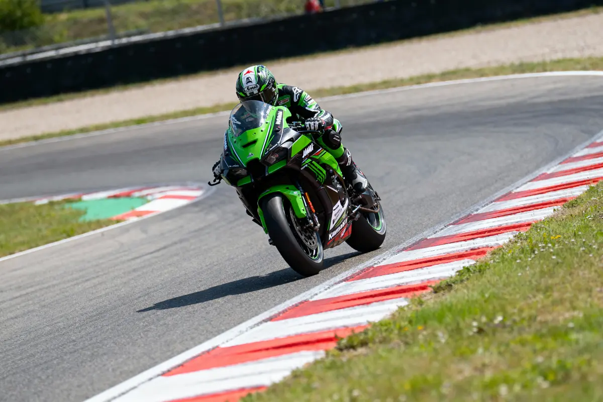 Moto verte en course sur circuit, pilote penché dans un virage, chaussée avec bordures rouges et blanches.