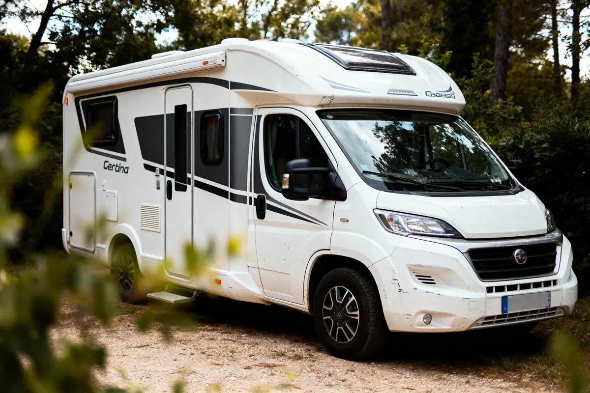 Camping-car blanc stationné en pleine nature, entouré d'arbres, sur un chemin de terre.