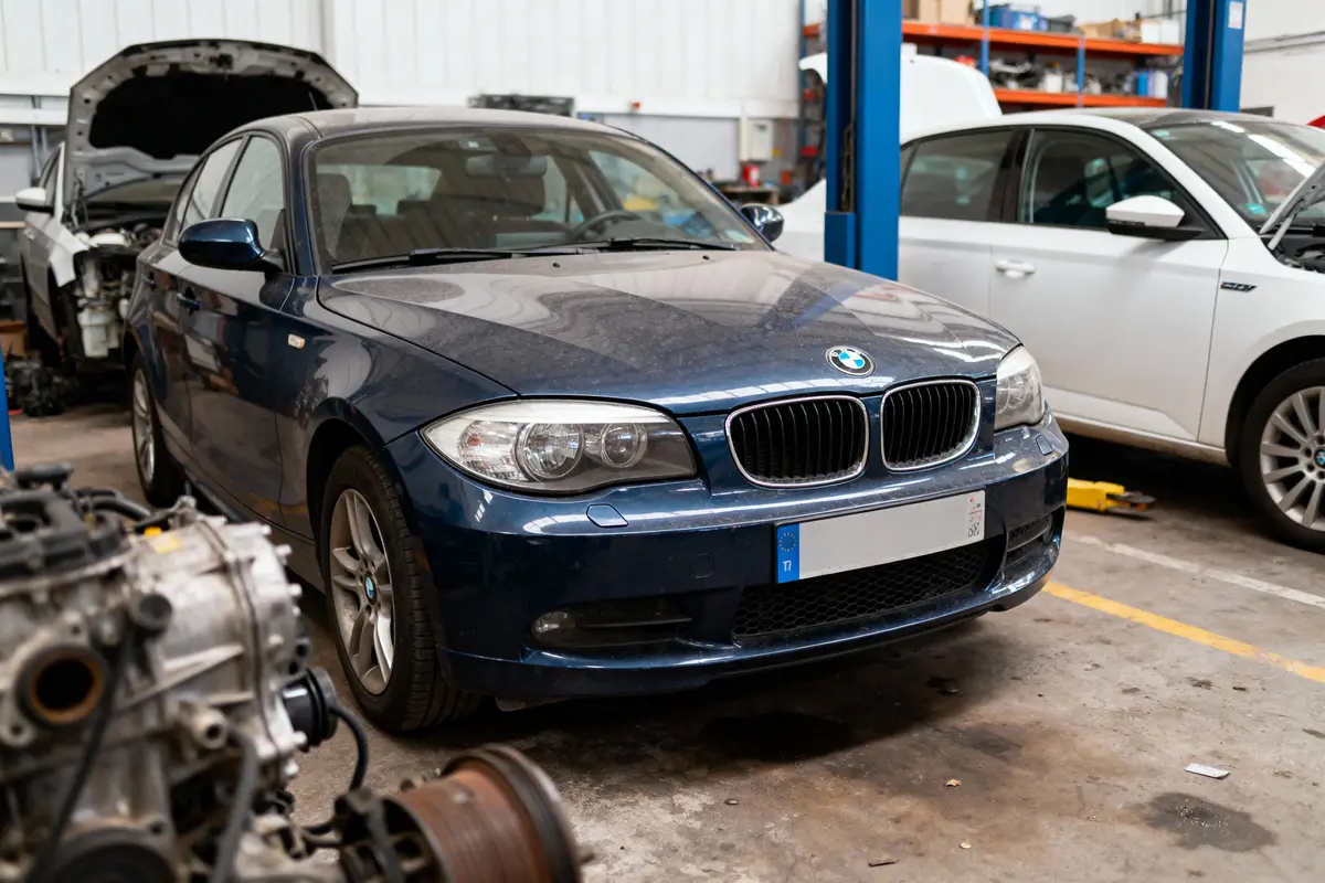 Voiture BMW bleue dans un garage, capot ouvert, moteur en réparation.