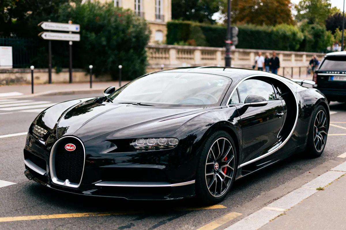 Voiture de sport noire, élégante, garée en ville, avec roues rouges et emblème visible. Environnement urbain en arrière-plan.