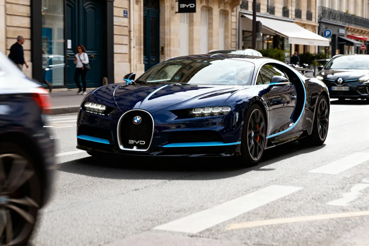 Voiture sportive bleue en ville, avec badge BMW, circulant sur une rue fréquentée.