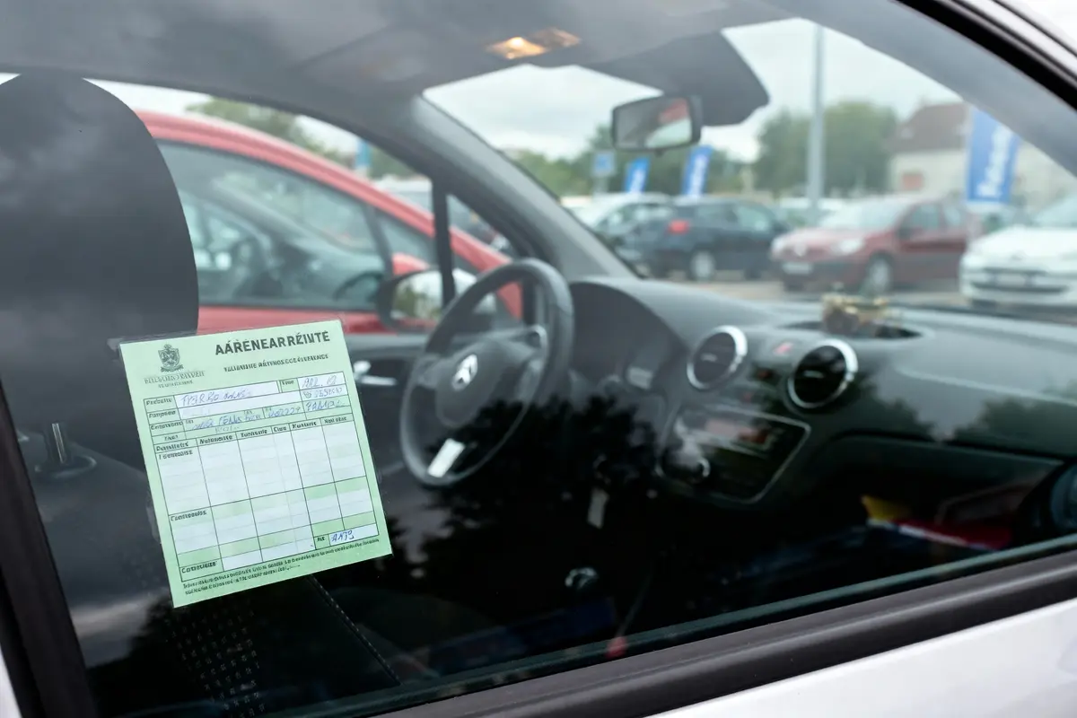 Voiture stationnée avec document vert sur le pare-brise, plusieurs véhicules visibles en arrière-plan flou.