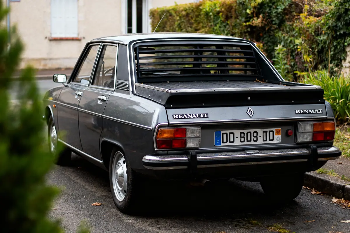 Voiture Renault classique grise, vue arrière, stationnée près de la bordure, maison en arrière-plan.