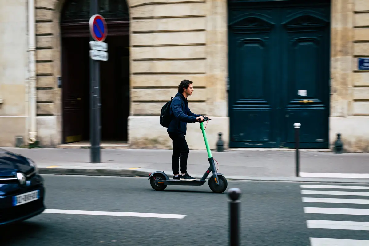 Personne en trottinette électrique verte sur une rue urbaine, passage piéton et bâtiments en arrière-plan.
