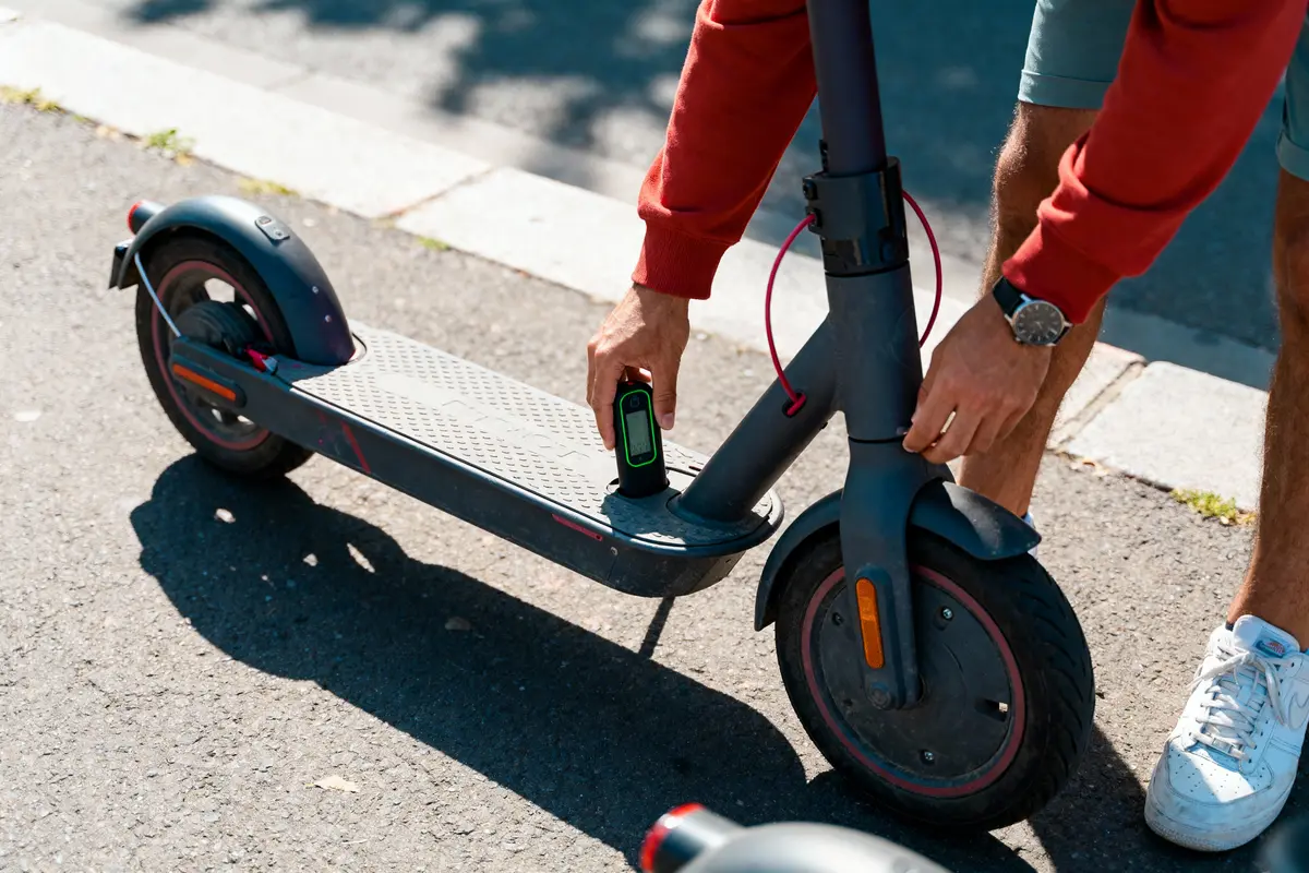 Homme installant une batterie sur une trottinette électrique, en extérieur, par une journée ensoleillée.
