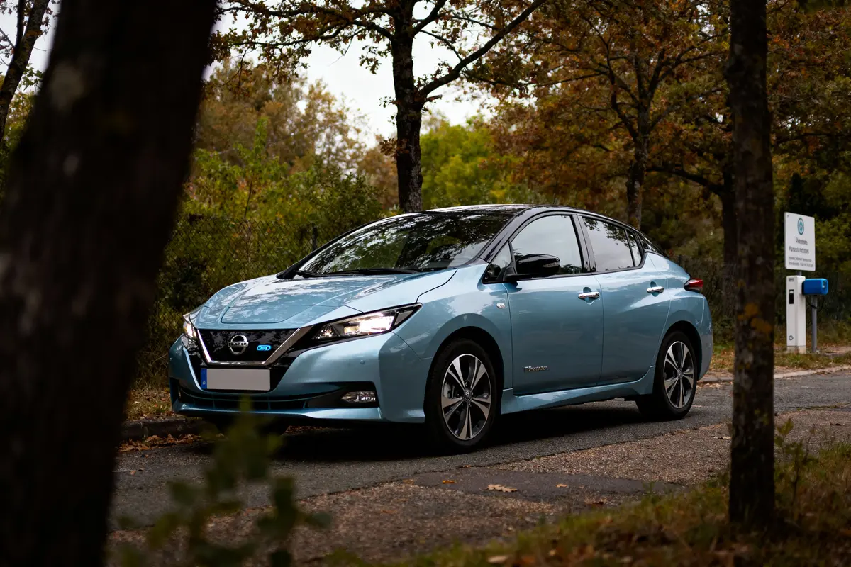 Voiture électrique bleue stationnée sur une route forestière, borne de recharge en arrière-plan.