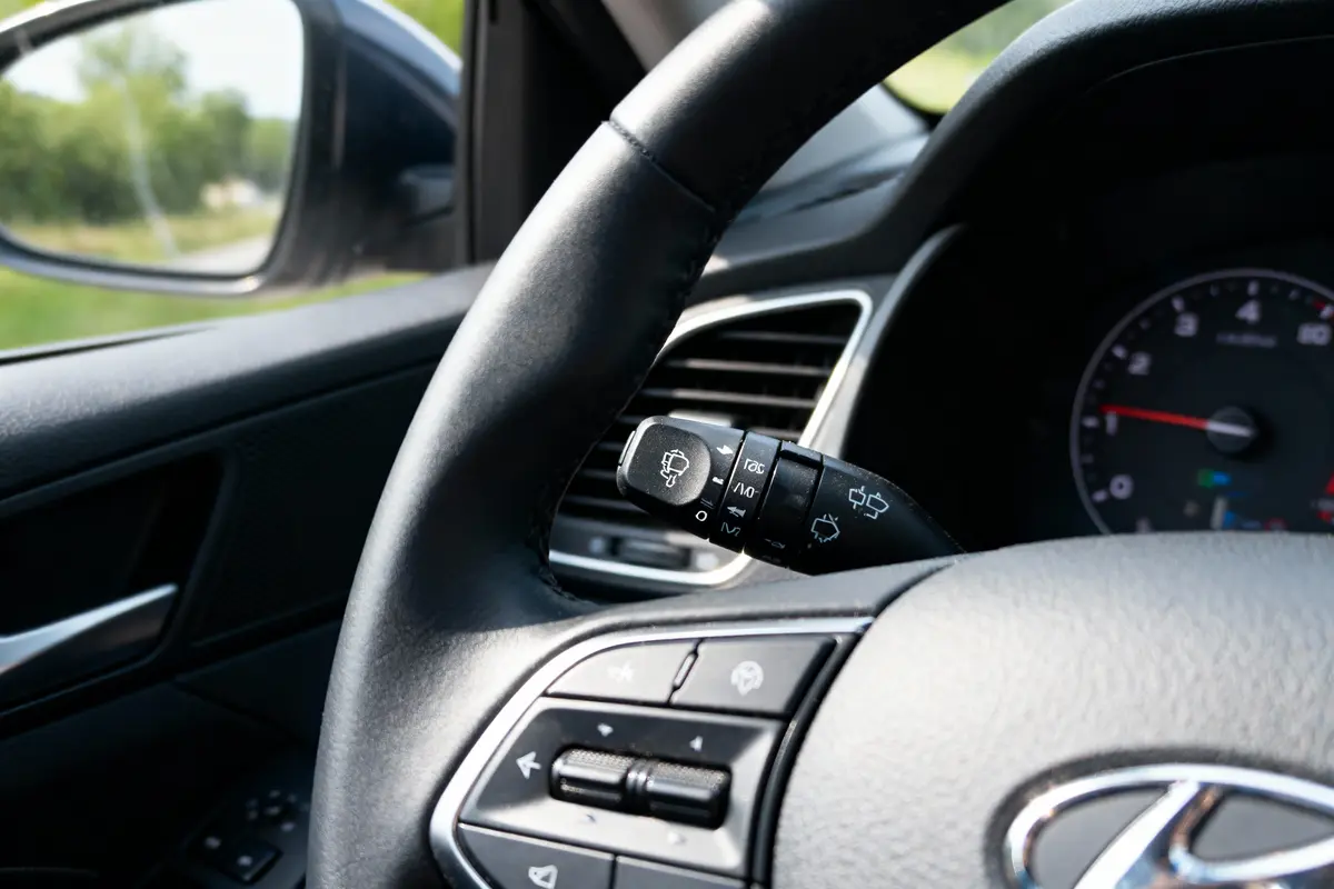 Volant de voiture avec commandes et levier de clignotants visible, vue intérieure.