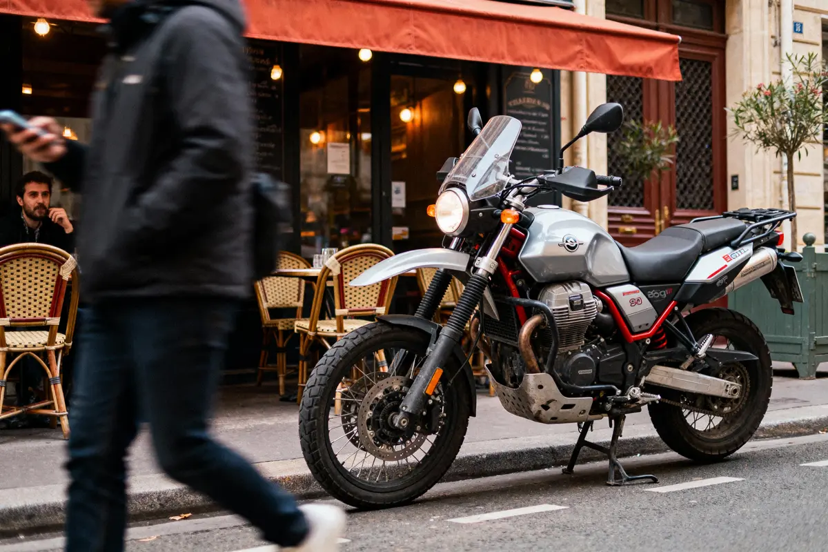 Une moto stationnée devant un café parisien, passant piéton flou, chaises en osier, ambiance urbaine.