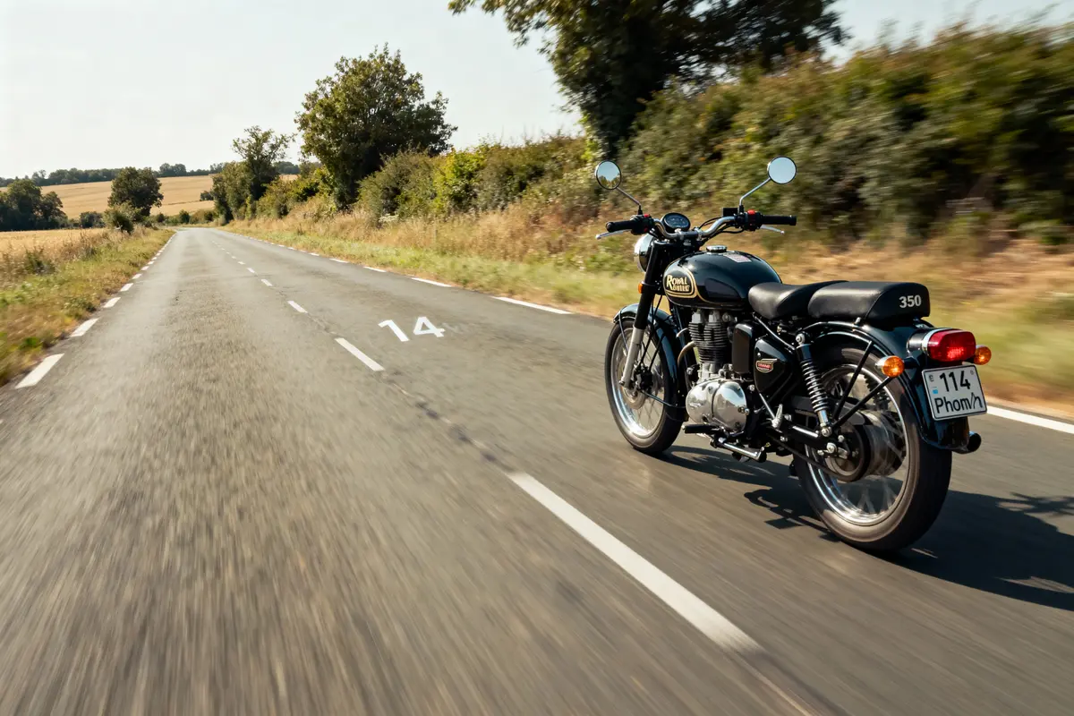 Moto Royal Enfield noire roulant sur route de campagne bordée d'arbres par temps clair et ensoleillé.