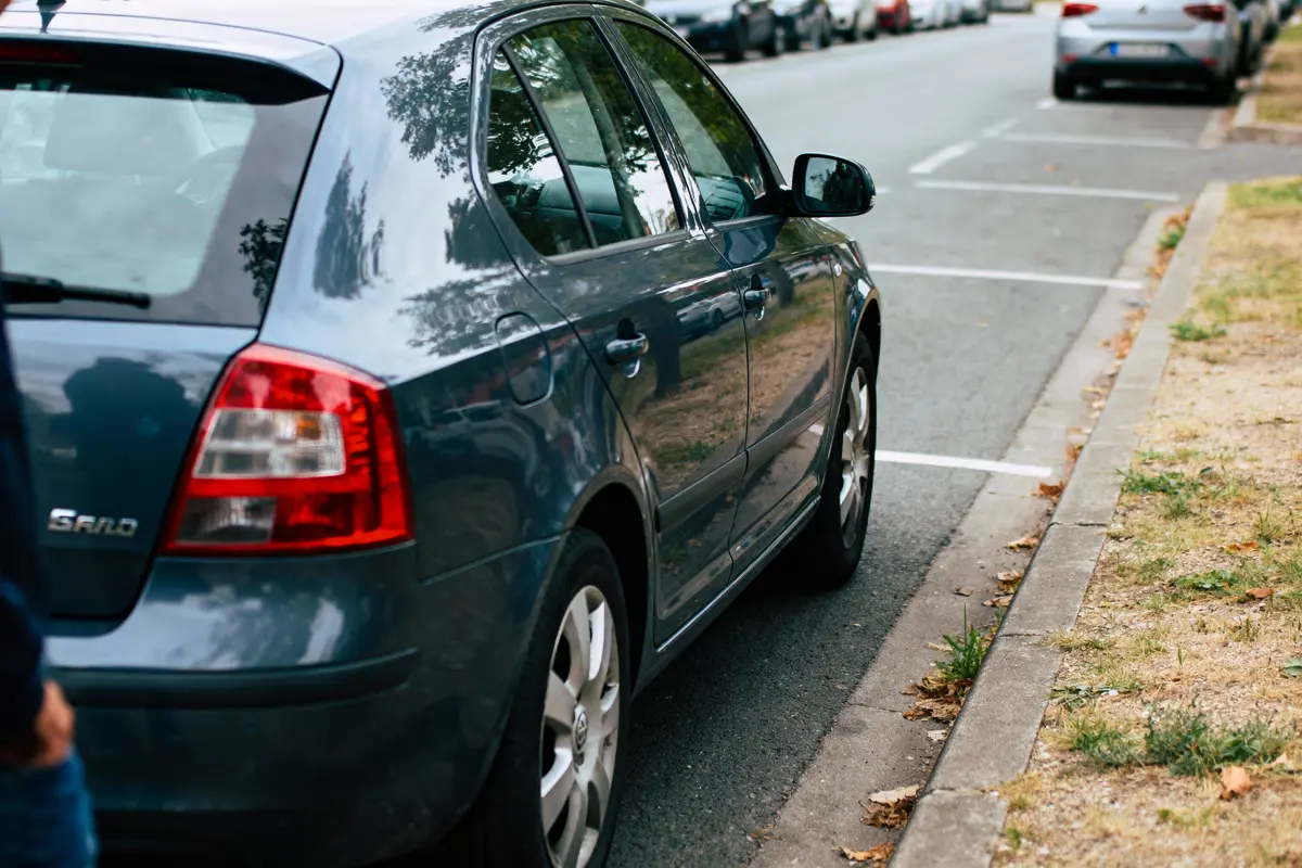 Voiture bleue garée le long d'une rue, avec trottoir et herbe environnante.