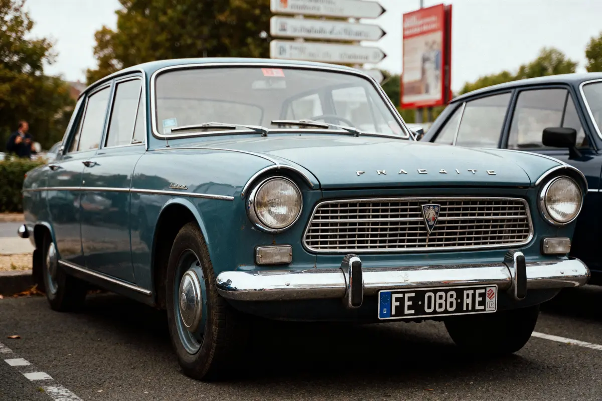 Voiture ancienne bleu foncé stationnée dans un parking, panneau de signalisation et végétation en arrière-plan.