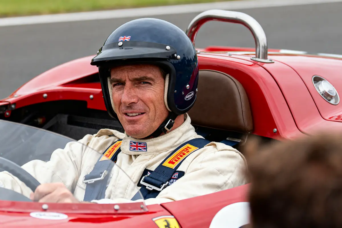 Pilote automobile portant un casque et combinaison, assis dans une voiture de course rouge, prêt pour la course.