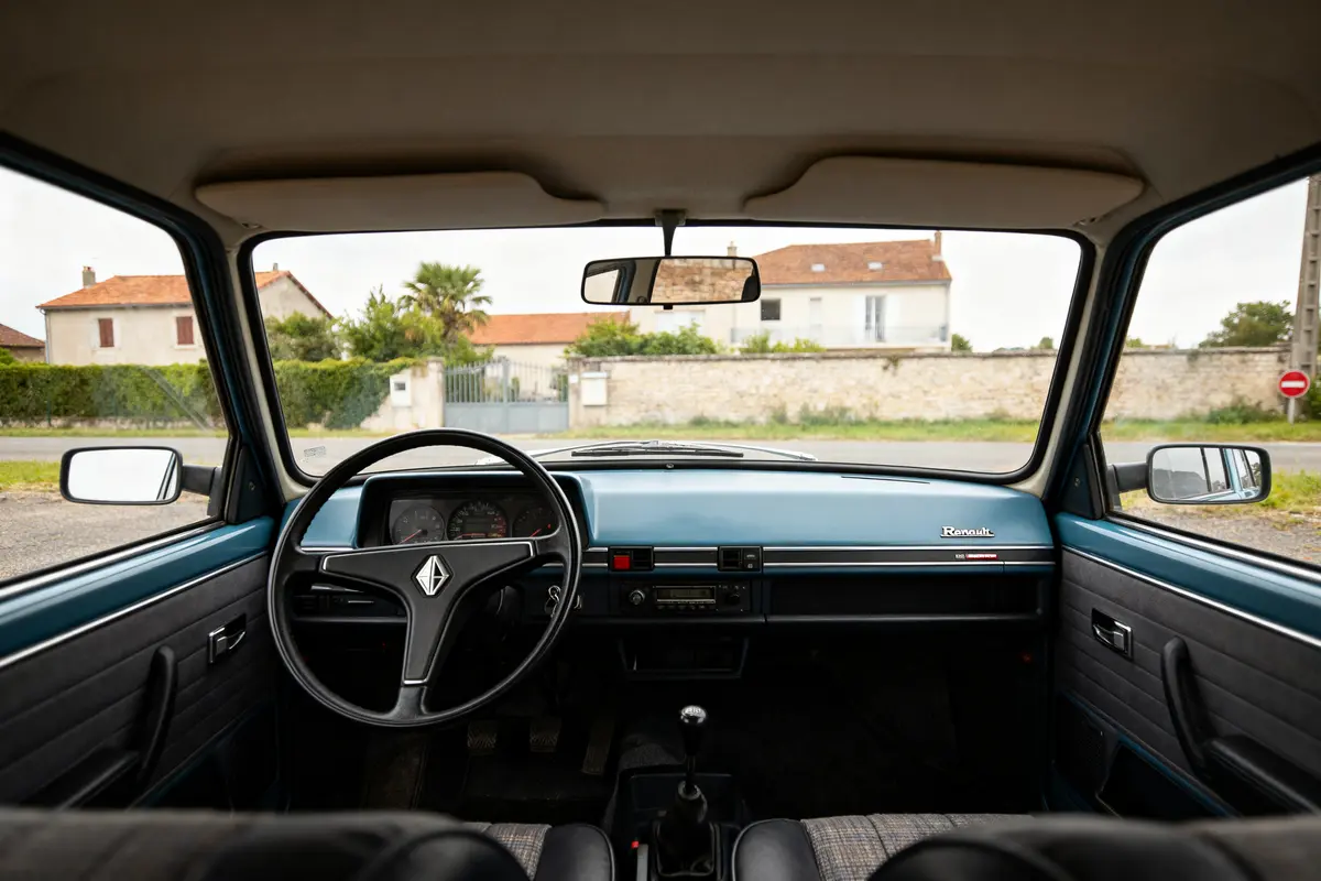 Intérieur de voiture vintage Renault avec vue sur l'extérieur résidentiel. Volant et tableau de bord visibles.