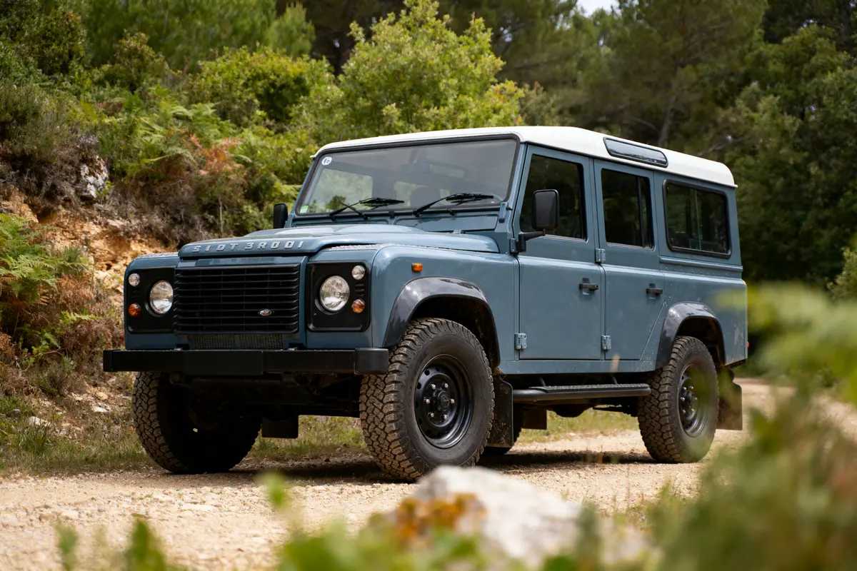 Jeep bleue conduite sur un chemin de terre, entourée de végétation luxuriante et sous-bois verdoyant.