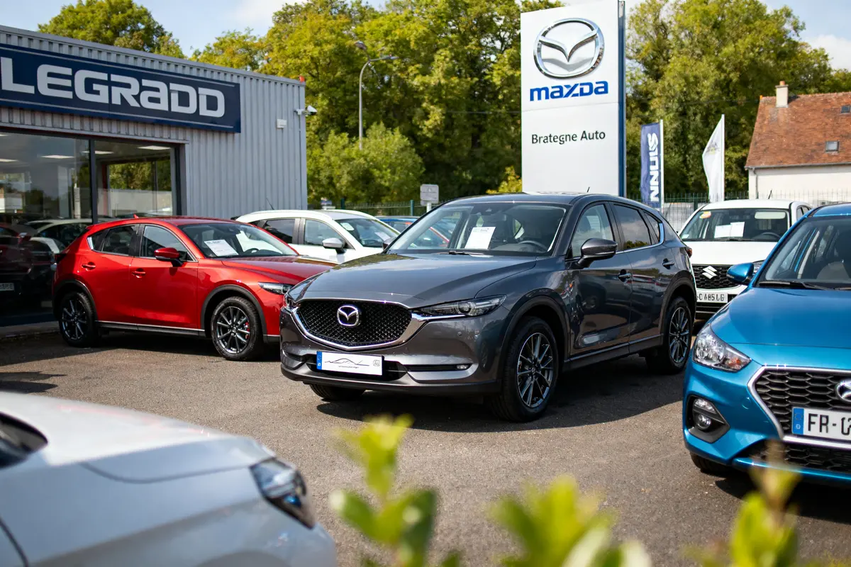 Voitures Mazda exposées dans une concession automobile, avec un panneau Mazda à l'arrière-plan.