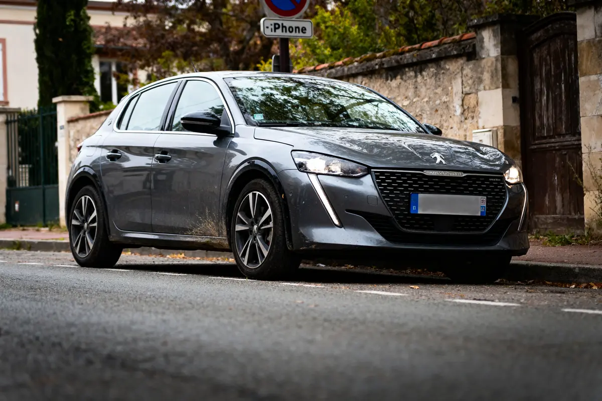 Voiture grise garée rue, devant mur en pierre, panneau "iPhone" en arrière-plan.