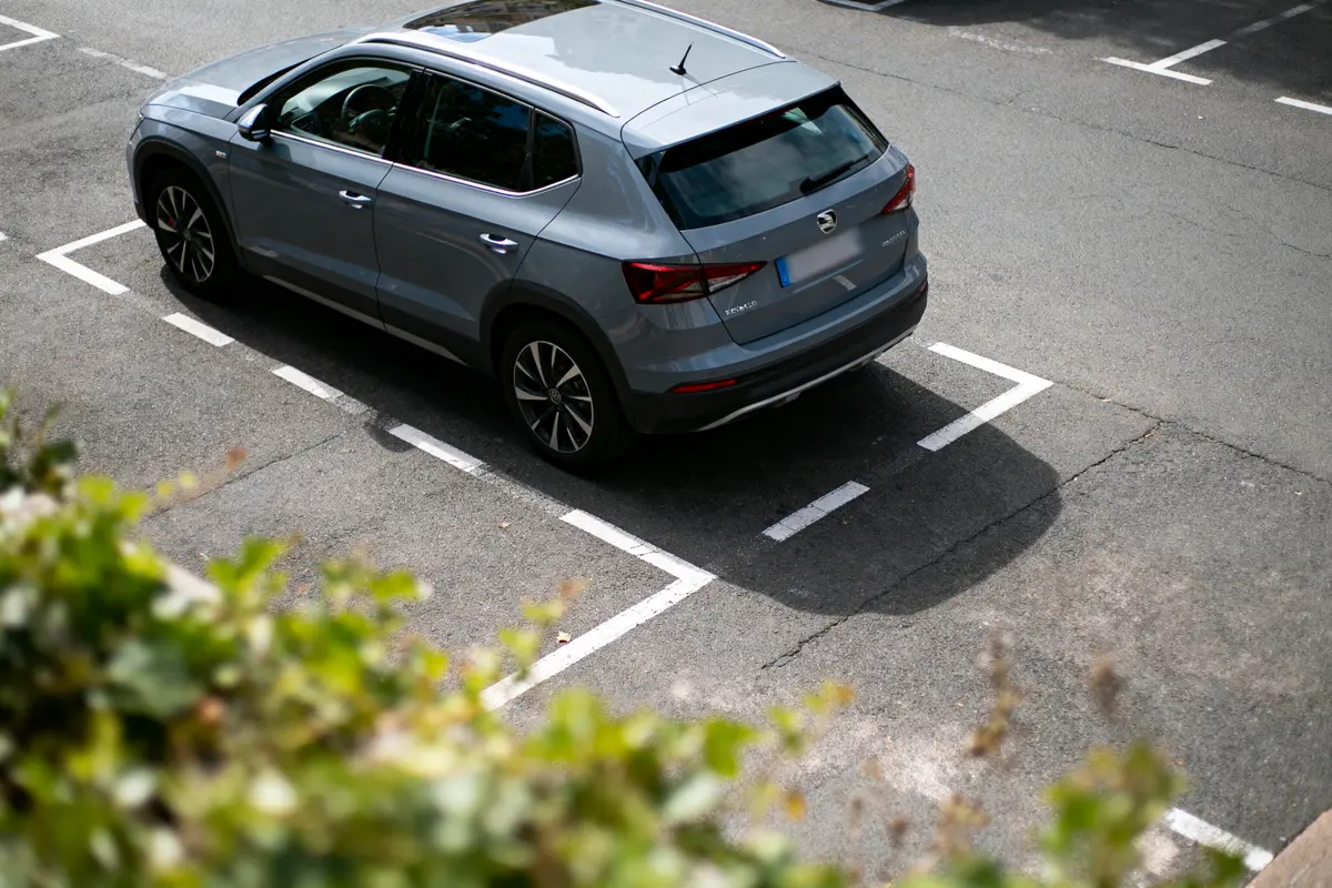 Voiture grise garée dans un parking, vue de dessus, avec feuillets verts au premier plan.