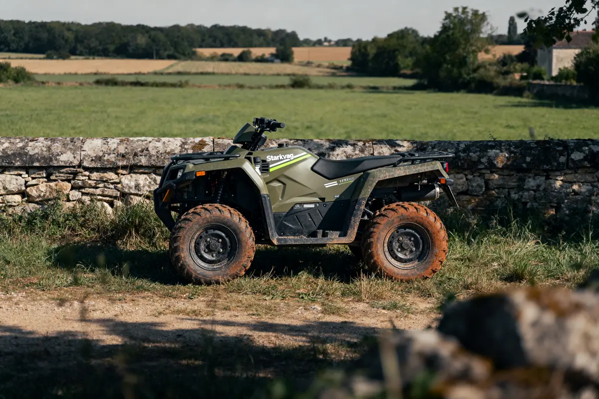 Quad vert garé devant un mur de pierres, avec un paysage champêtre en arrière-plan.