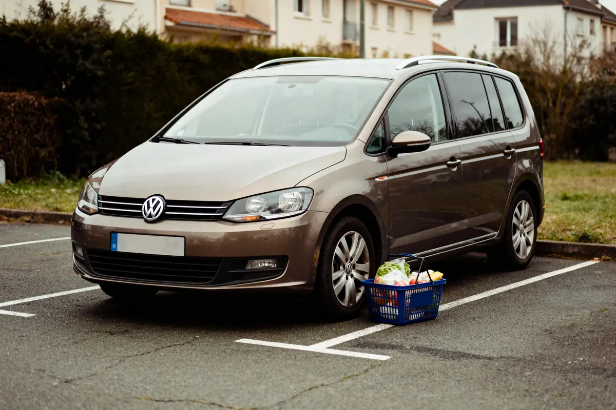 Voiture Volkswagen grise garée sur un parking avec un panier de courses au sol.