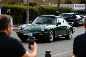 Voiture Porsche verte passant devant le panneau Caradisiac lors d'un événement automobile.