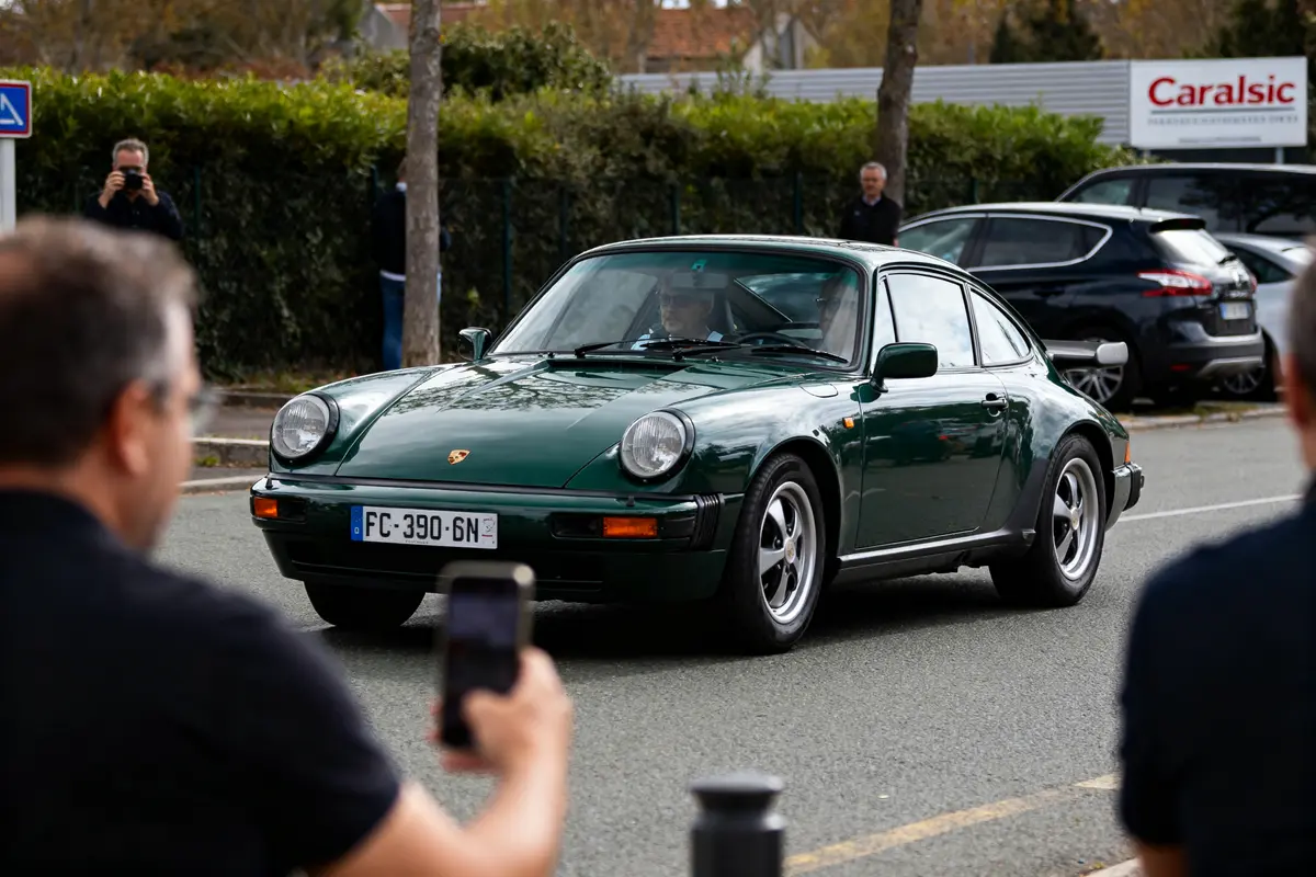 Voiture Porsche verte passant devant le panneau Caradisiac lors d'un événement automobile.