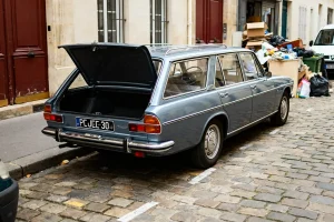 Peugeot 304 Estate bleu garée avec coffre ouvert sur rue pavée et déchets à côté
