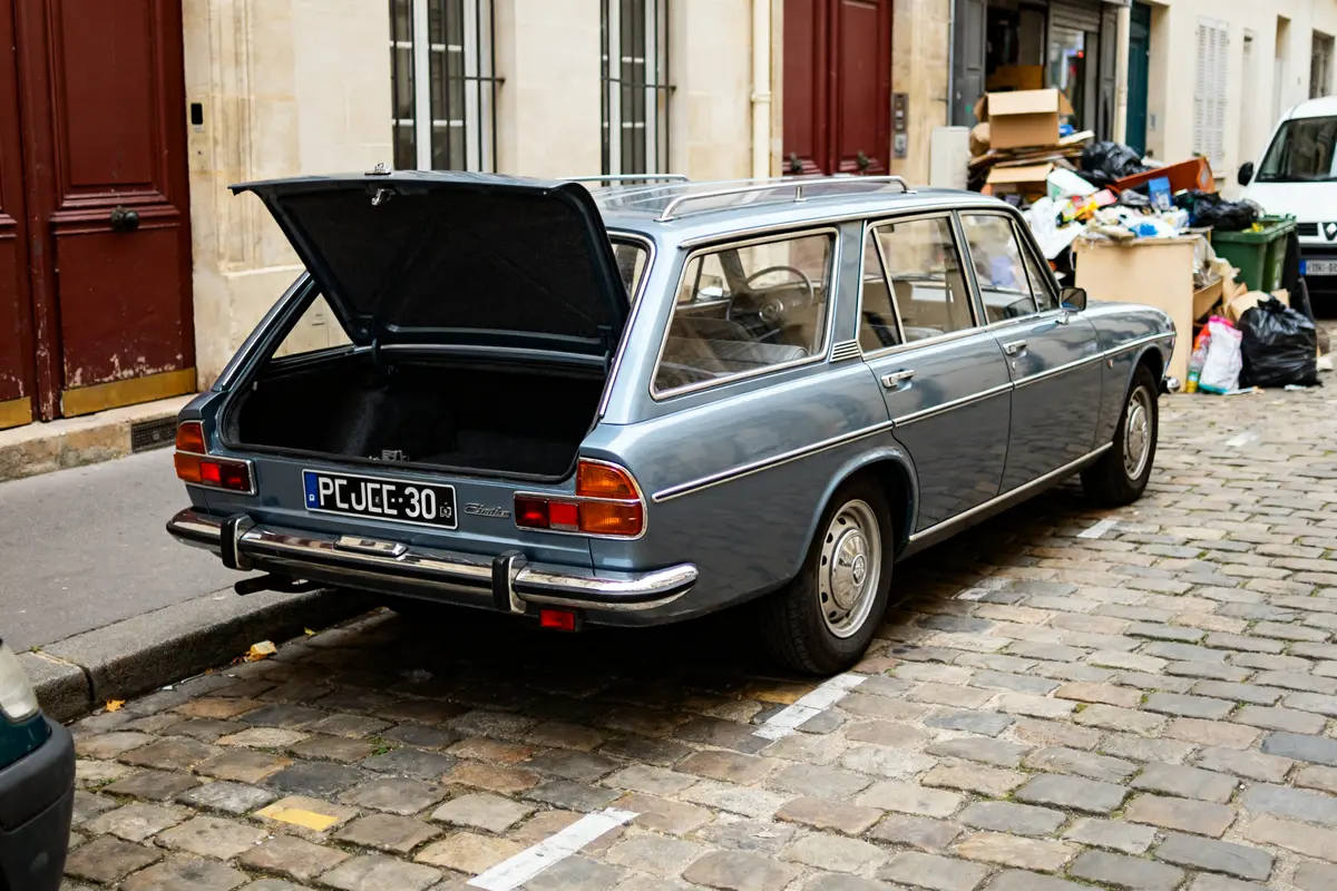 Peugeot 304 Estate bleu garée avec coffre ouvert sur rue pavée et déchets à côté