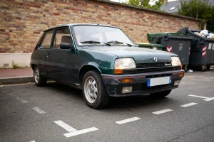 Renault 5 thermique verte garée près de poubelles sur un parking urbain