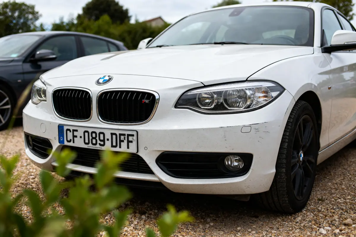 Voiture blanche bmw série 1 f20 modèle à éviter stationnée sur un parking gravillonné