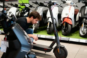 Un homme examine une trottinette électrique devant une rangée de scooters exposés.