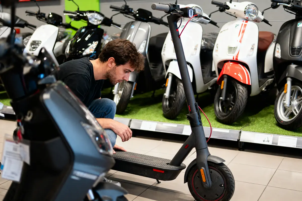 Un homme examine une trottinette électrique devant une rangée de scooters exposés.