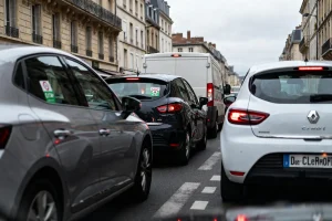 Embouteillage urbain avec voitures et camion sur une rue bordée d'immeubles anciens. Atmosphère nuageuse.