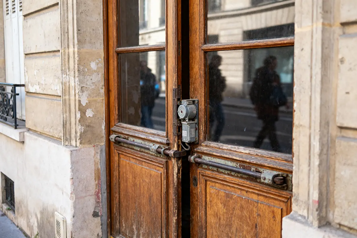 Porte en bois ancienne avec serrure métallique, reflets de personnes en mouvement dans la vitre.