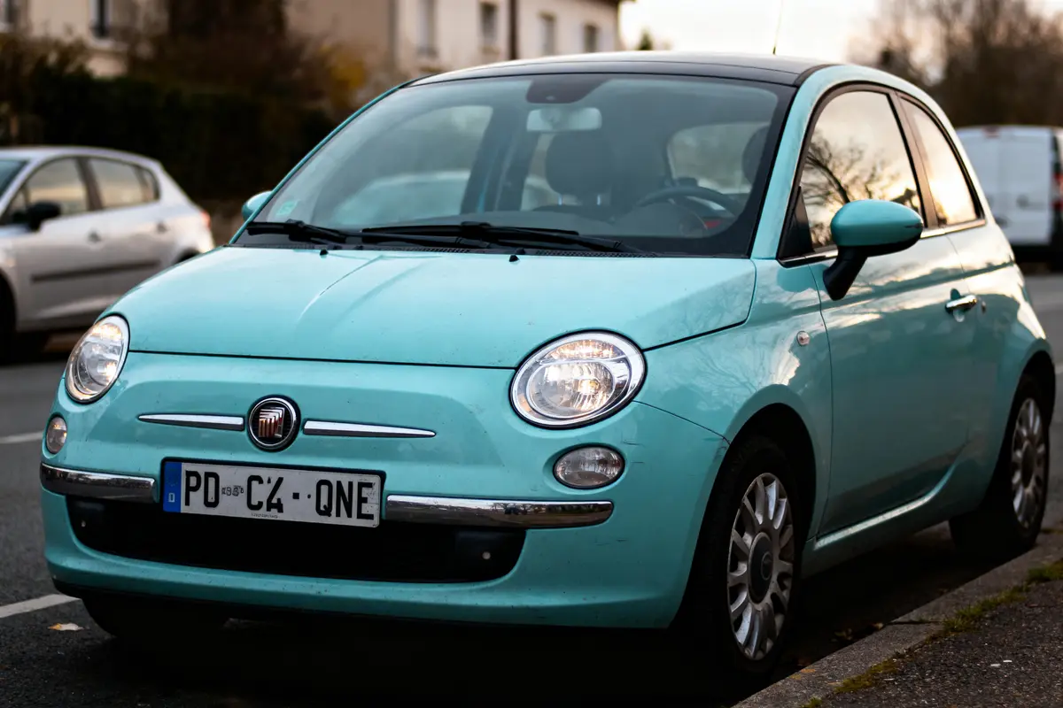 Voiture Fiat 500 turquoise garée dans la rue, prise de vue diagonale avant gauche.