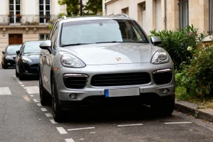 SUV argenté garé en ville, entouré de végétation, bâtiments en arrière-plan.