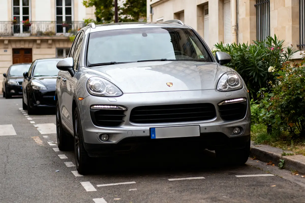 SUV argenté garé en ville, entouré de végétation, bâtiments en arrière-plan.