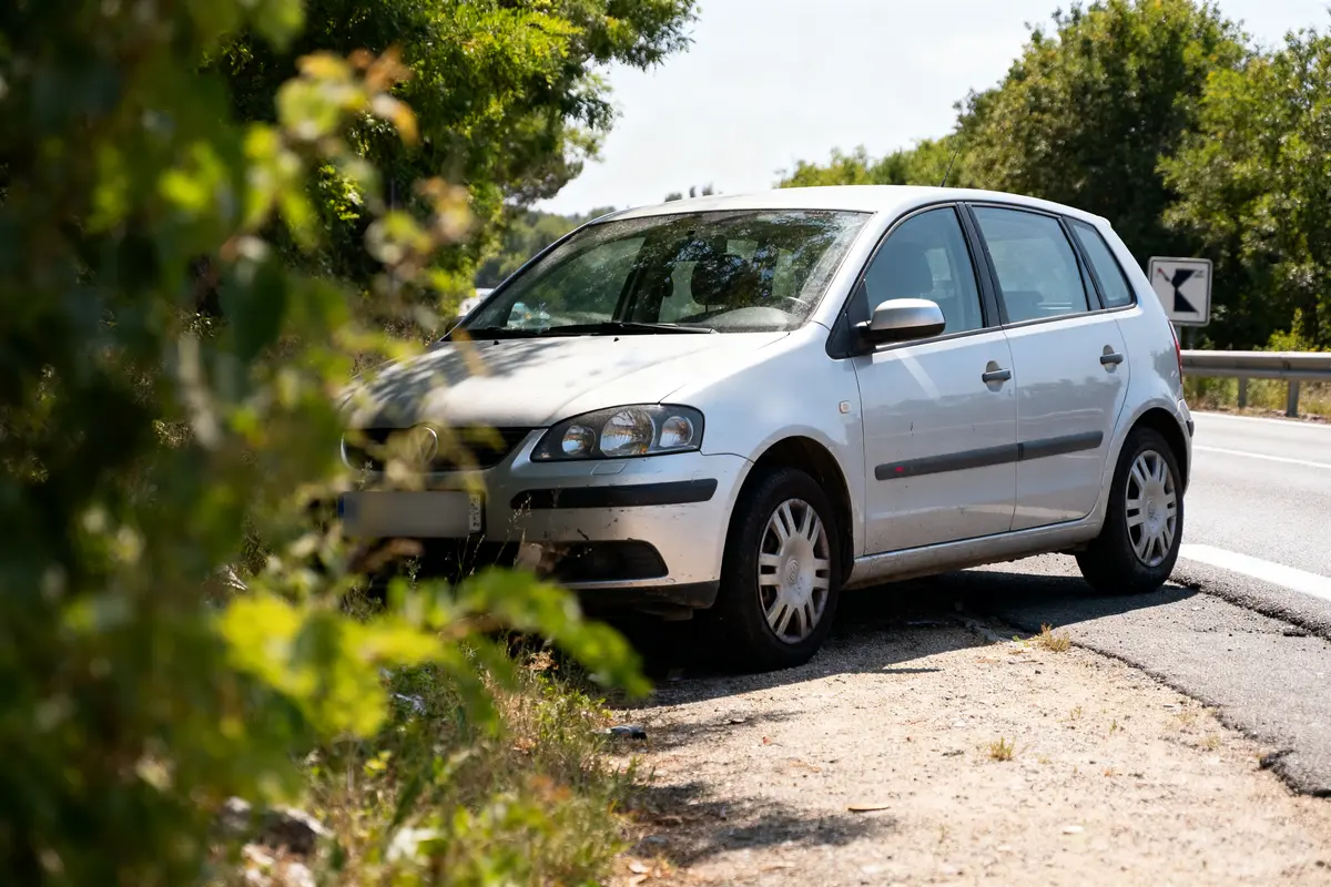 Voiture blanche garée sur le bas-côté d'une route, entourée de végétation verte.