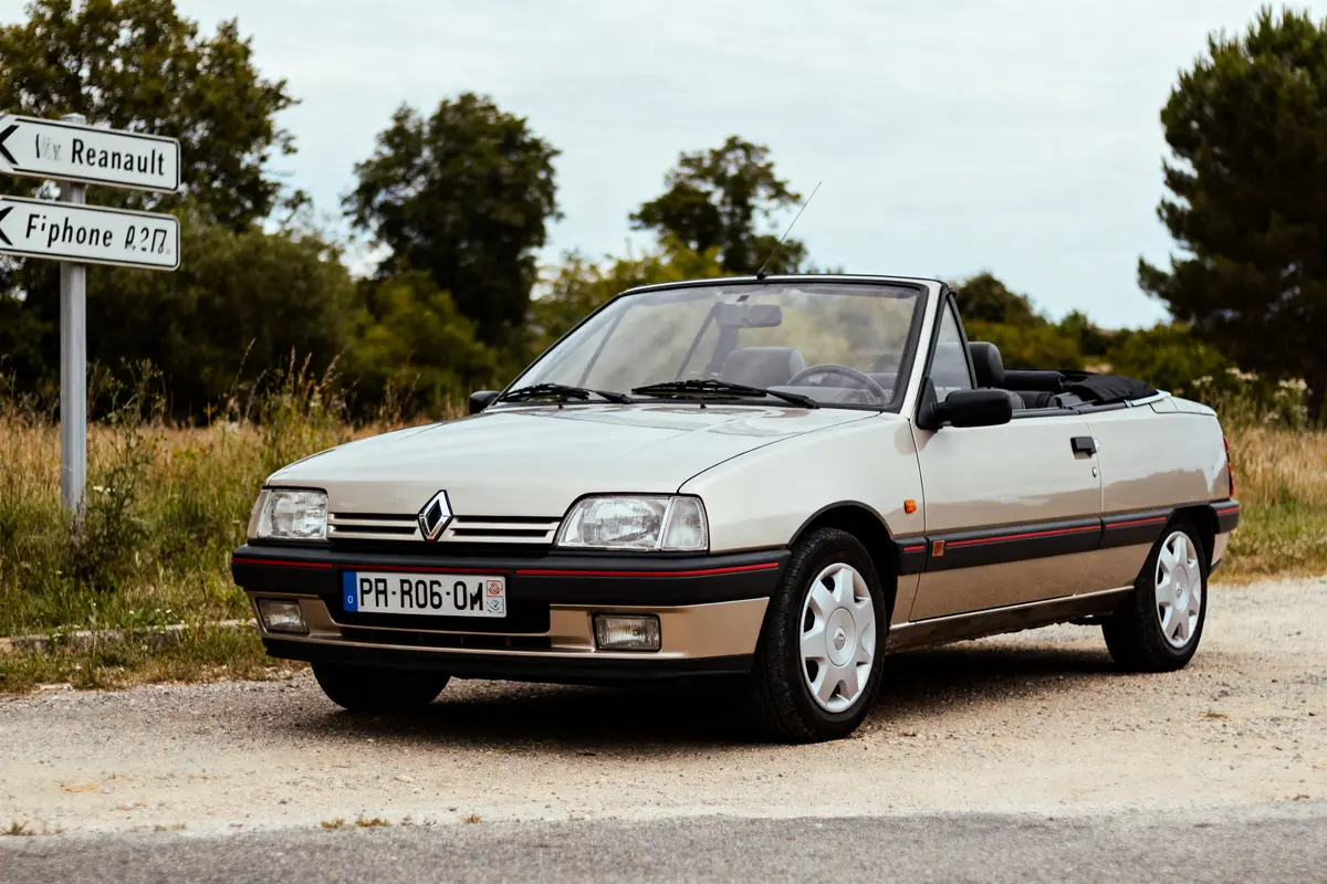 Voiture décapotable Renault ancienne, stationnée près de panneaux sur route de campagne, arbres en arrière-plan.