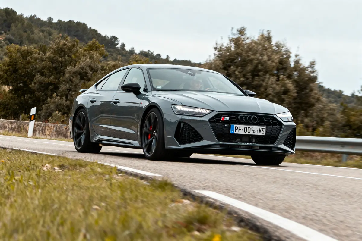 Voiture sportive grise Audi RS roulant sur route sinueuse avec paysage arboré en arrière-plan.