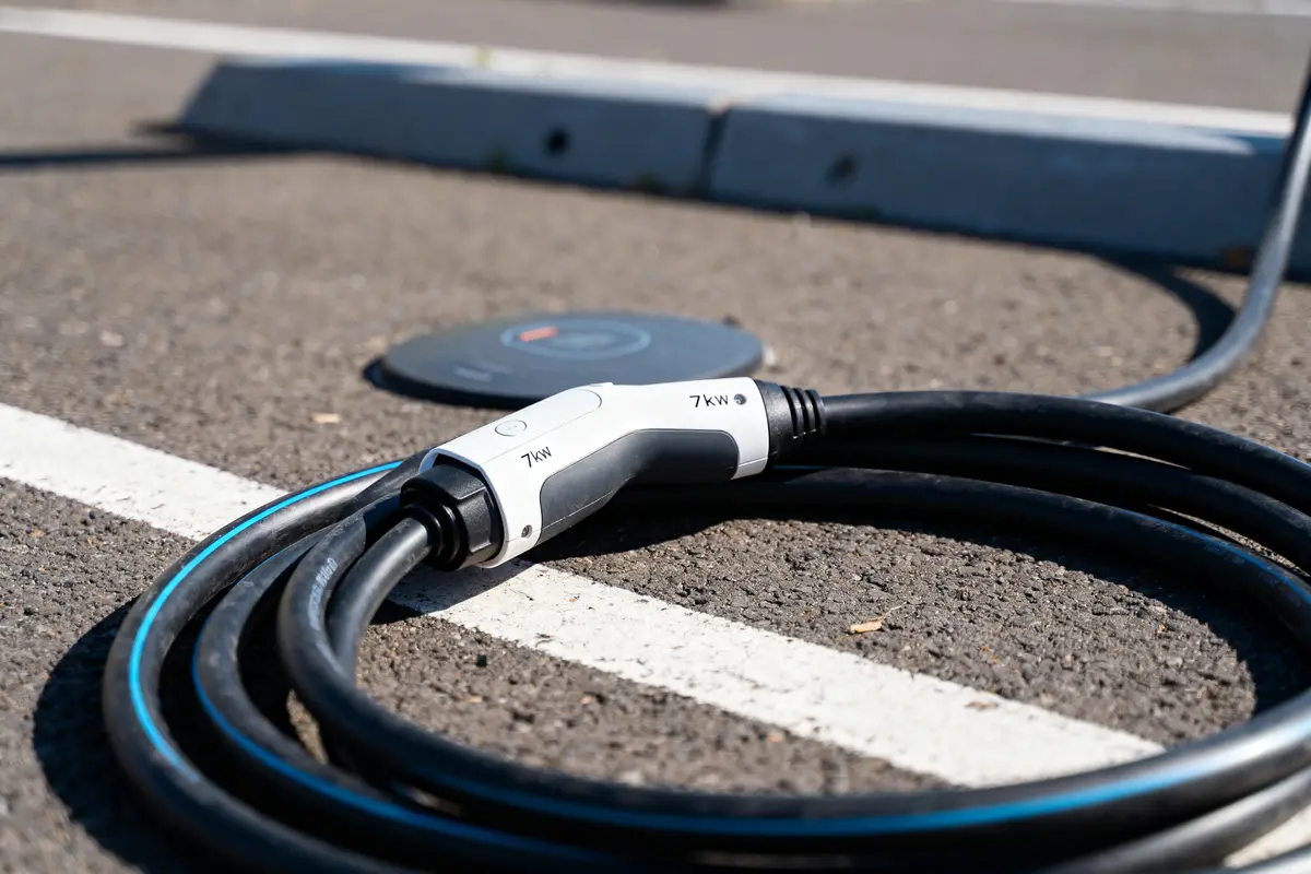Câble de recharge électrique 7kW sur un parking asphalté, près d'une station de chargement.