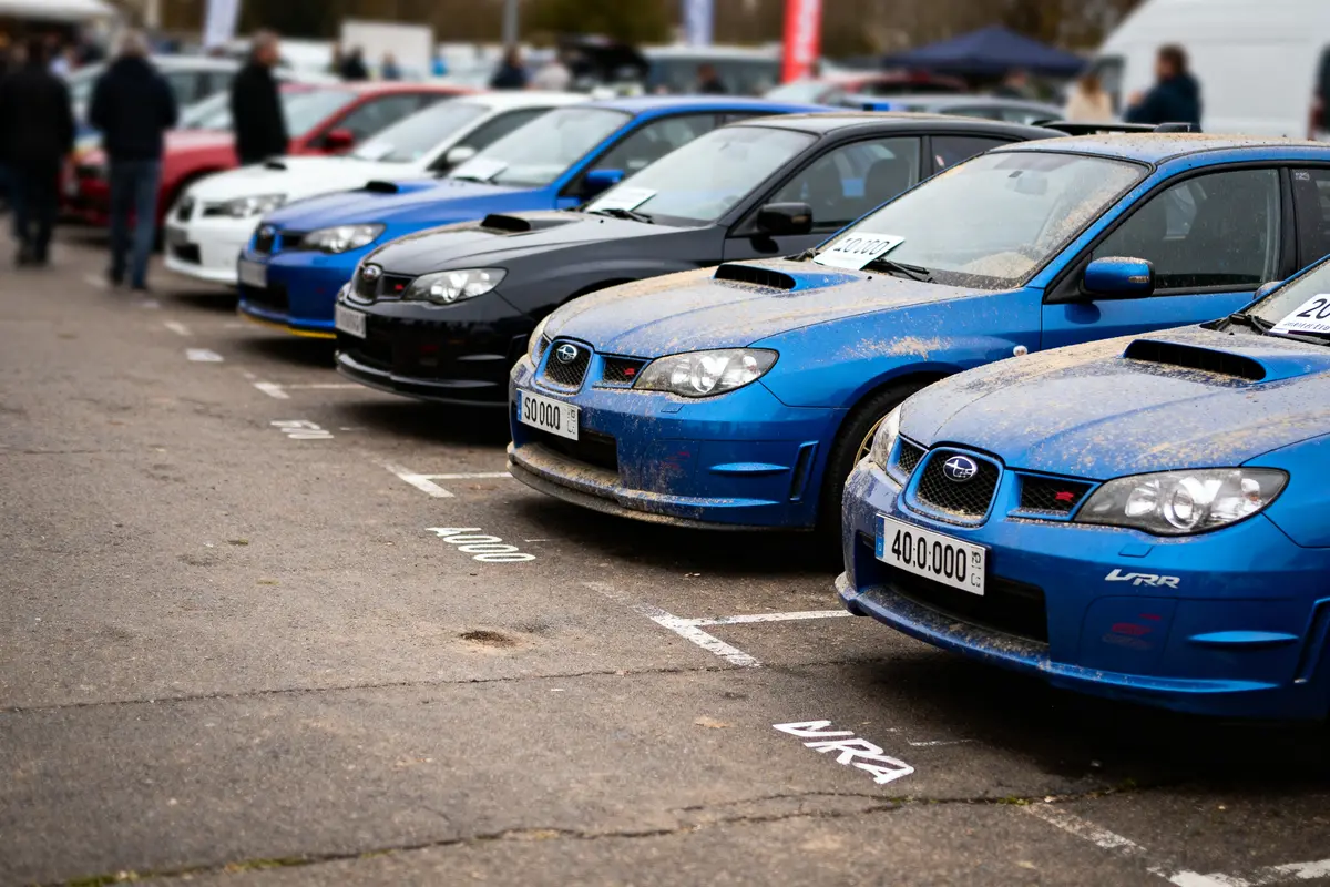 Voitures Subaru bleues alignées, exposées dans un stationnement, ambiance de rassemblement automobile.