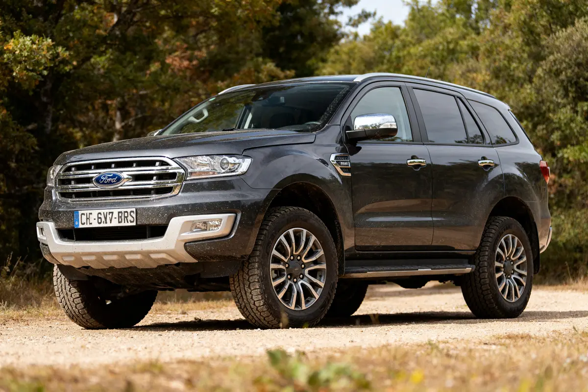 SUV noir Ford Everest garé sur un chemin de terre avec des arbres à l'arrière-plan
