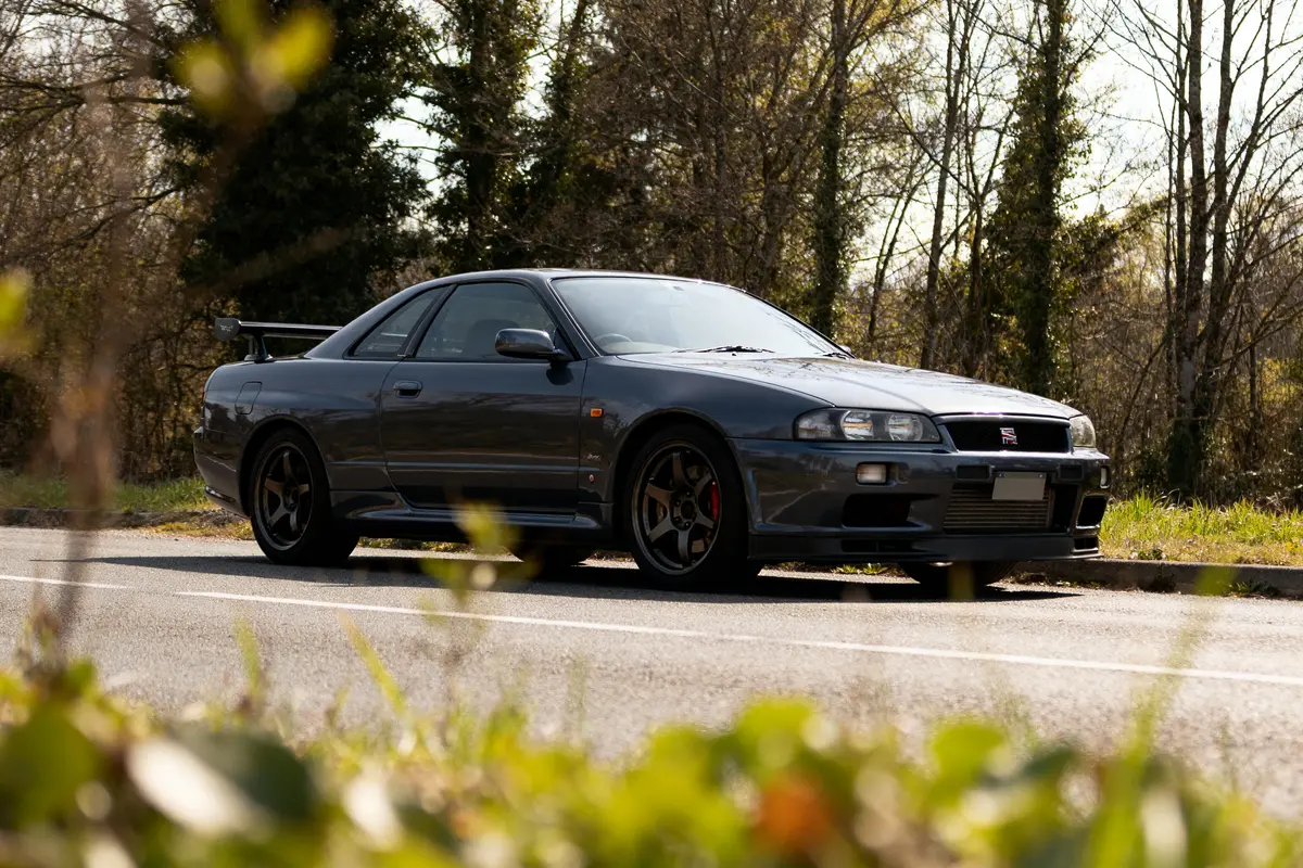 Berline R34 Skyline garée sur route entourée de végétation et d'arbres en arrière-plan