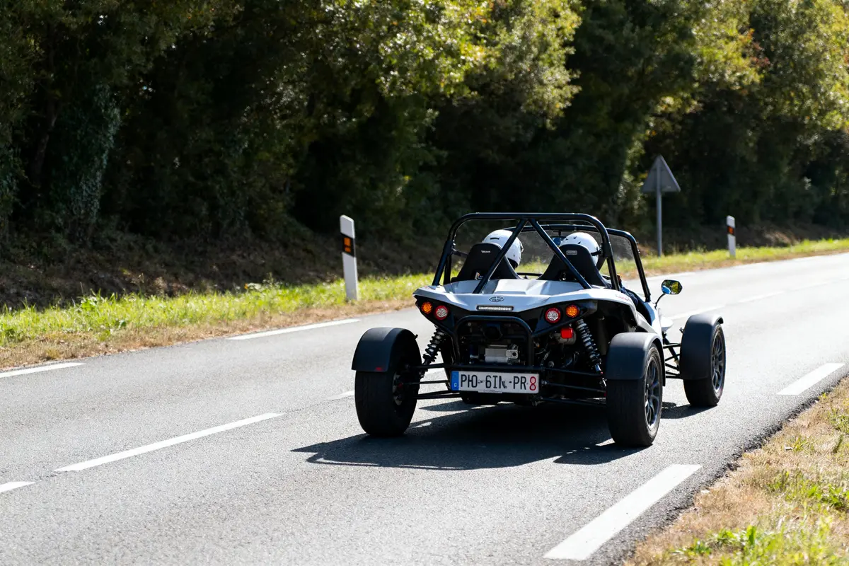 Buggy homologué circulant sur route ensoleillée, entouré de végétation dense.